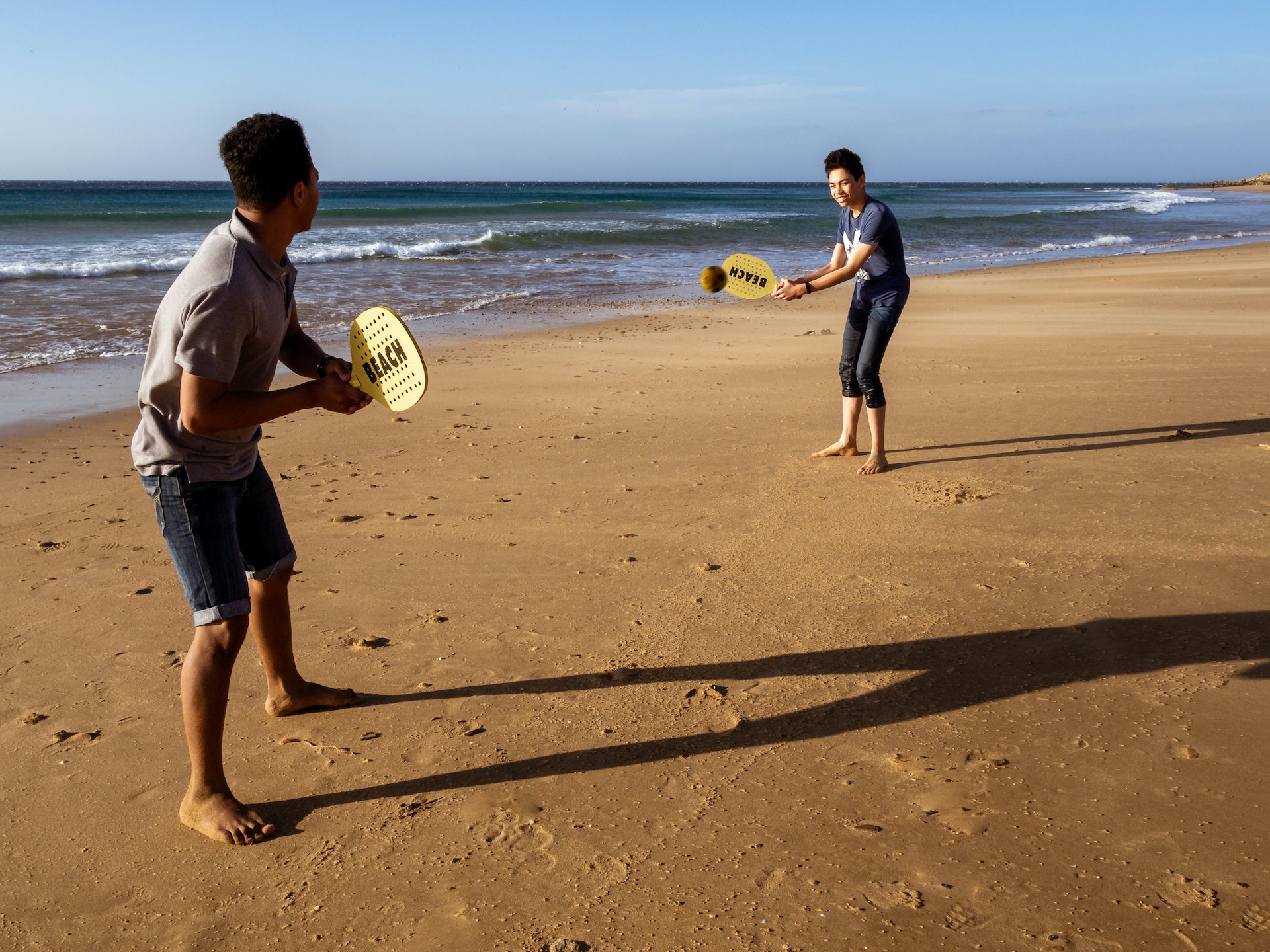 Deux adolescents souriants jouent au ballon de raquette sur le sable orange de la plage d'Achakar à Tanger, Maroc