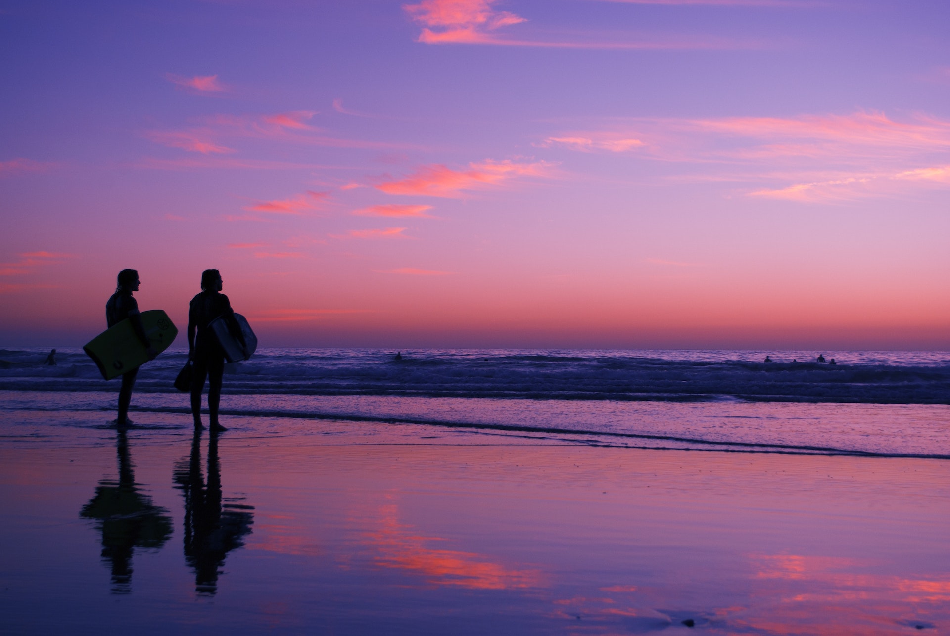 Dans un tourbillon d'orange et de violet alors que le soleil disparaît, deux silhouettes de surfeurs se tiennent sur la plage de Taghazout au Maroc et arpentent la mer